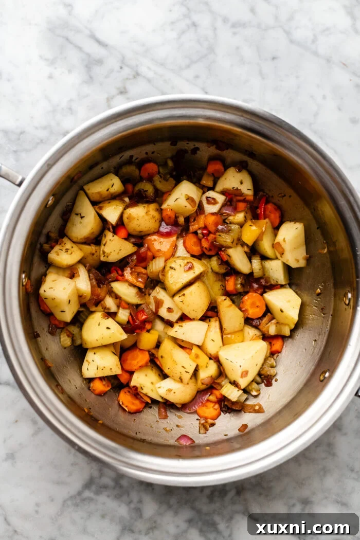 Diced Yukon Gold potatoes being gently softened with other vegetables in a large pot.