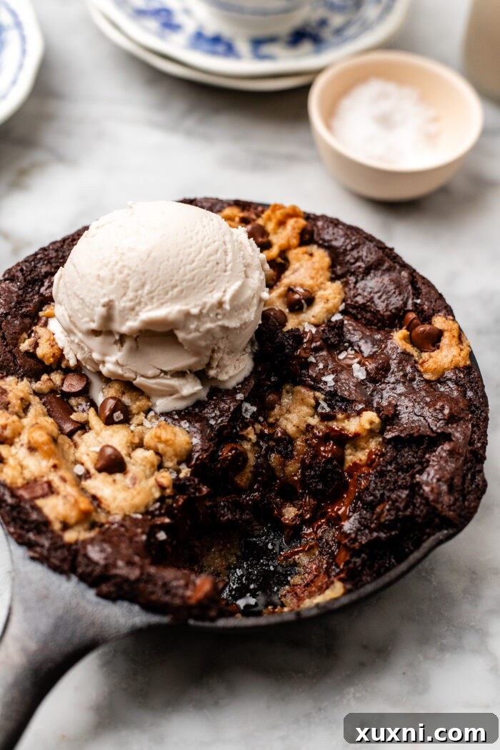 Molten mini brookie cookie skillet with a scoop taken out, revealing creamy dairy-free Nutella filling, served on marble.