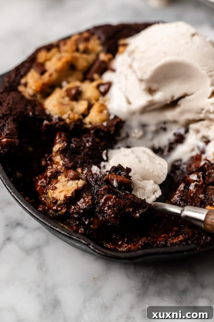 Scooped section of a warm mini brookie cookie skillet, showcasing the layers of brownie and cookie dough with a melted 'Nutella' core, ready to be enjoyed.