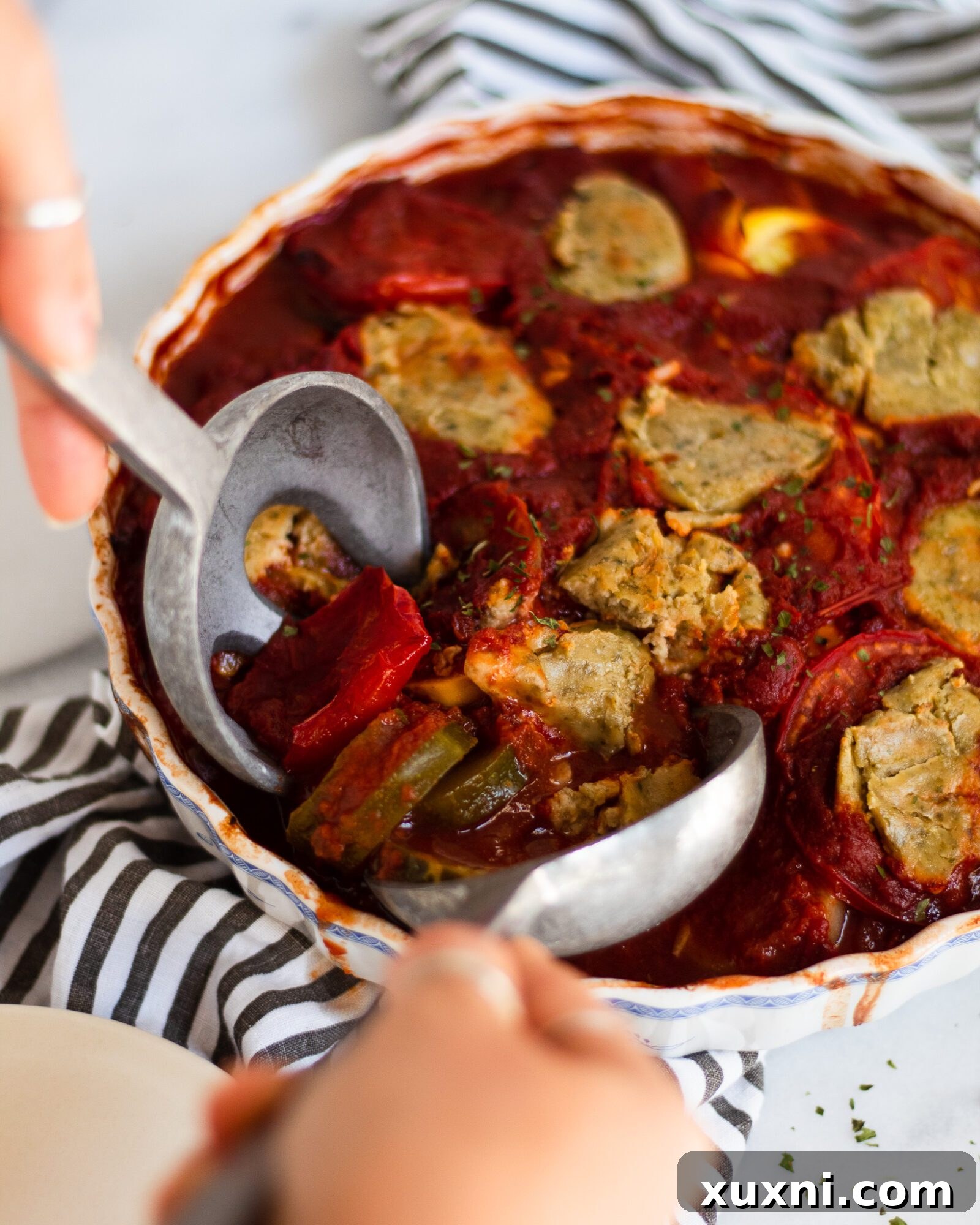 Hands scooping a generous portion of freshly baked ratatouille from a casserole dish