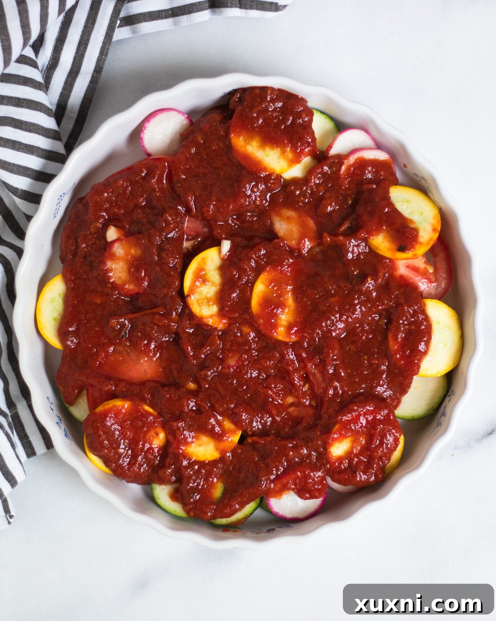 Tomato puree spread over fresh vegetables in a baking dish, preparing for baking
