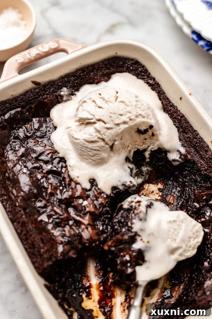 A close-up of a spoon digging into the warm, gooey small-batch vegan brownie pudding, garnished with melting vegan vanilla ice cream.