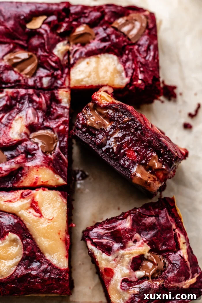 A tray of perfectly sliced vegan red velvet brownies with visible cheesecake swirls and crinkle tops.