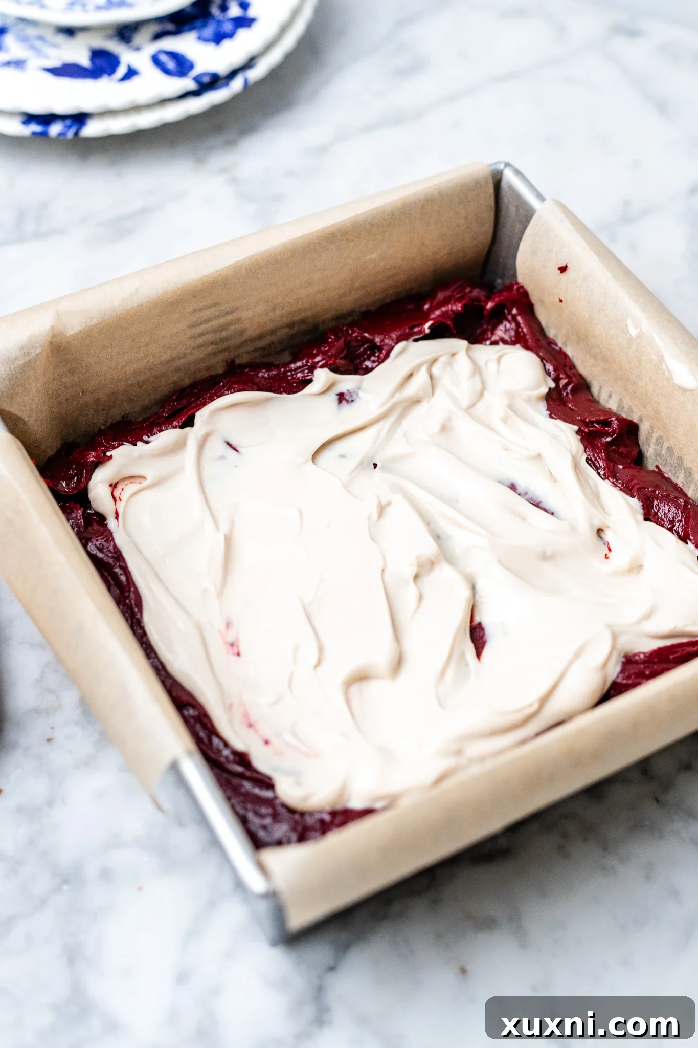 Assembling vegan red velvet brownies with cheesecake swirl in a baking pan.