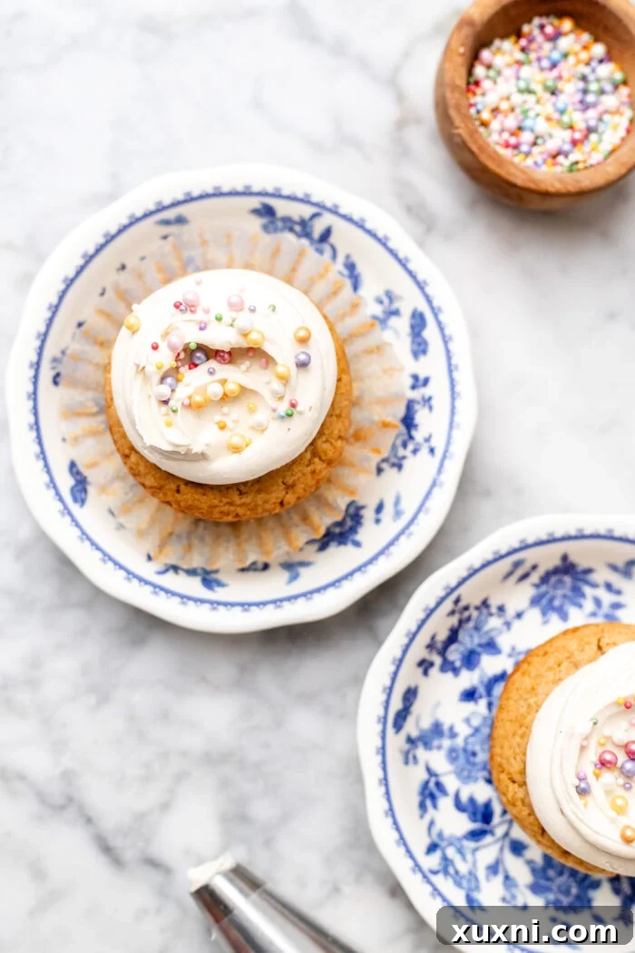 two vegan vanilla cupcakes on plates, beautifully frosted and ready to enjoy