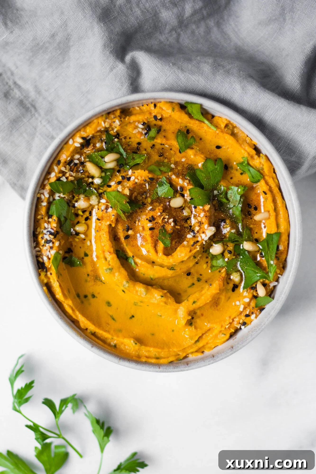 Bowl of creamy healthy sweet potato hummus, garnished with herbs and a drizzle of olive oil.