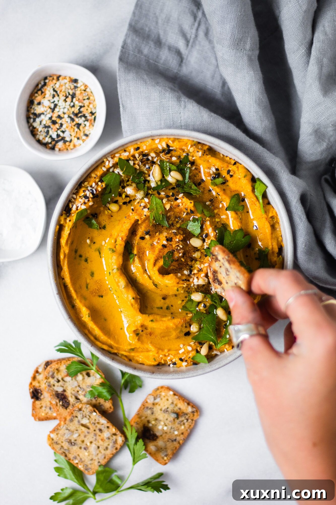 Hand dipping a cracker into a bowl of healthy sweet potato hummus, showcasing its creamy texture.