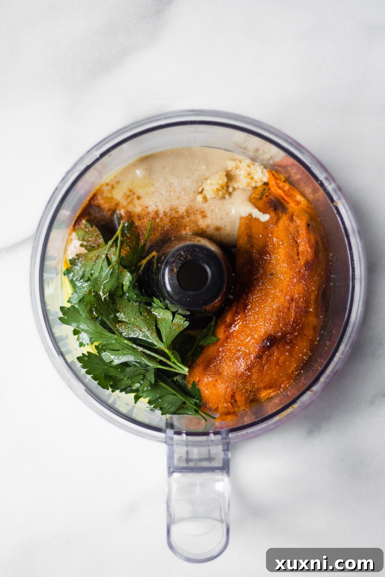 Sweet potato hummus ingredients being added to a food processor, ready for blending.