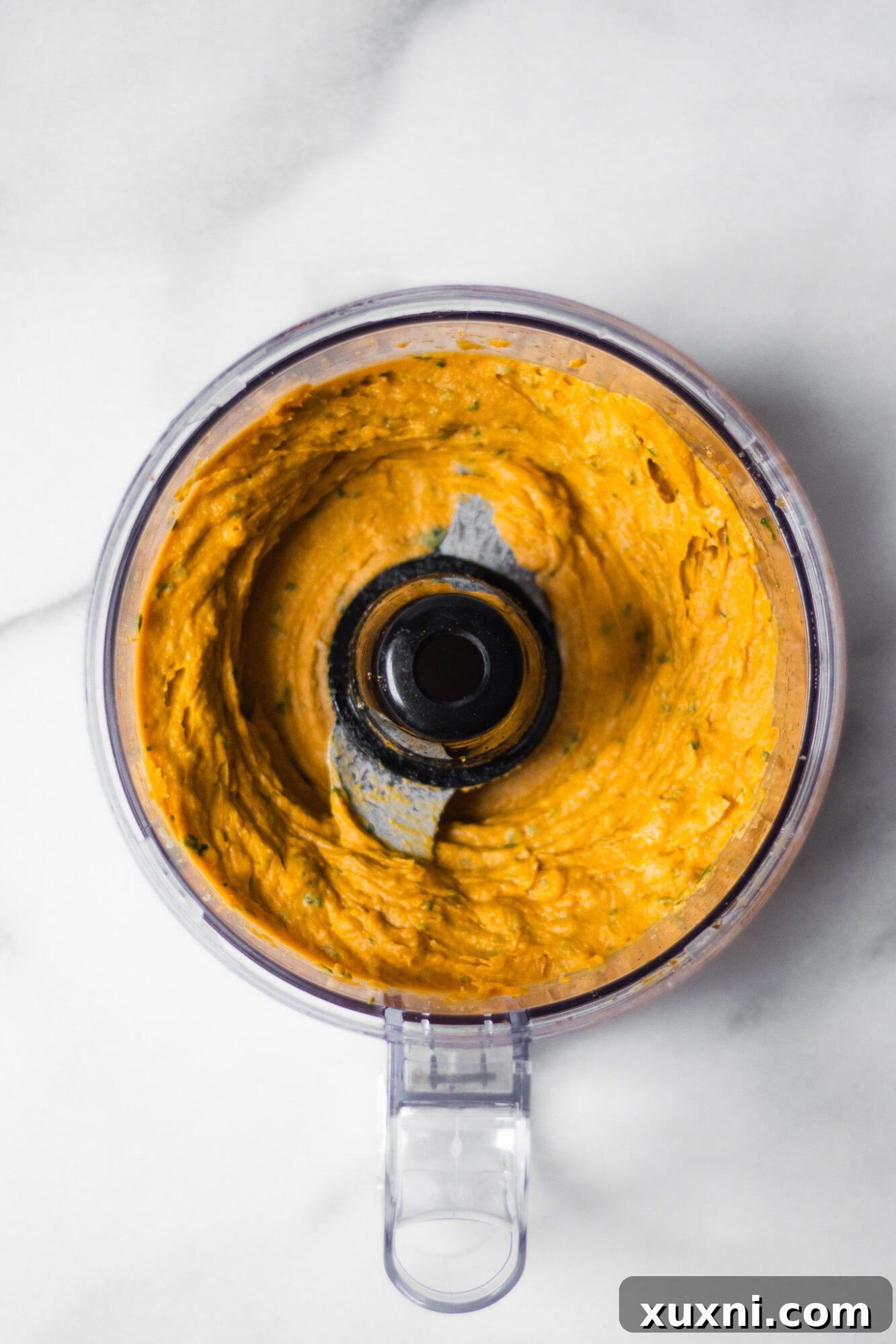 Blended smooth sweet potato hummus in a food processor, ready to be scooped and served.