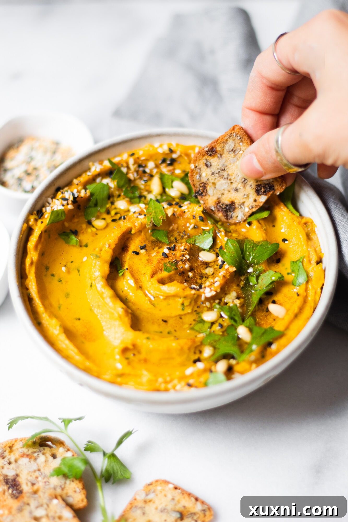 Hand dipping a cracker into the rich and creamy sweet potato hummus.
