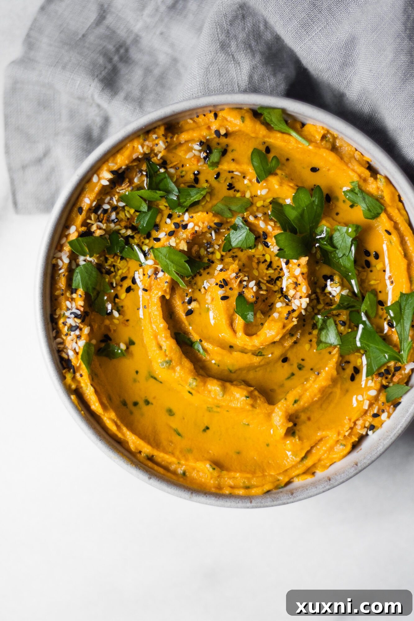 Close-up of homemade sweet potato hummus in a bowl, garnished with herbs and a swirl of olive oil.