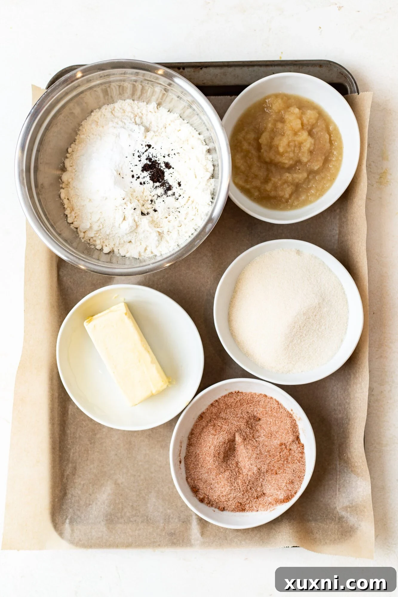 A selection of ingredients laid out for making vegan snickerdoodles, including flour, vegan butter, and applesauce.