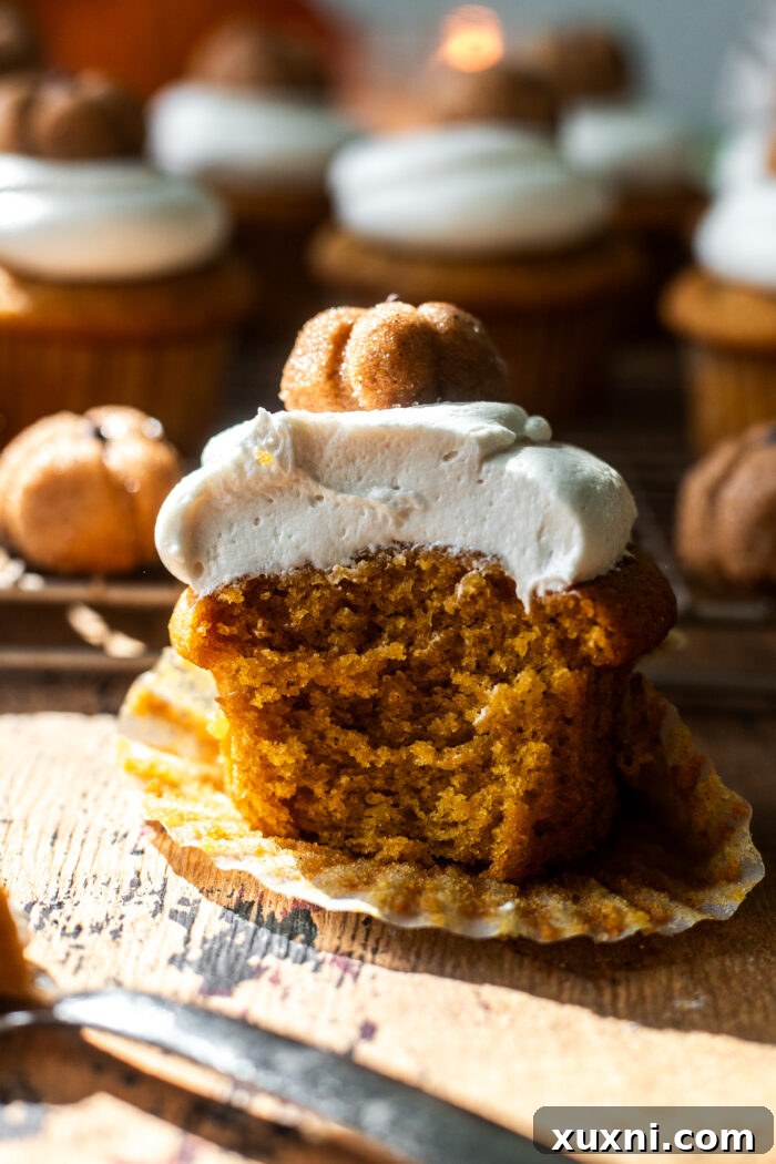 Bitten vegan pumpkin cupcake with cream cheese frosting, showing its moist interior.