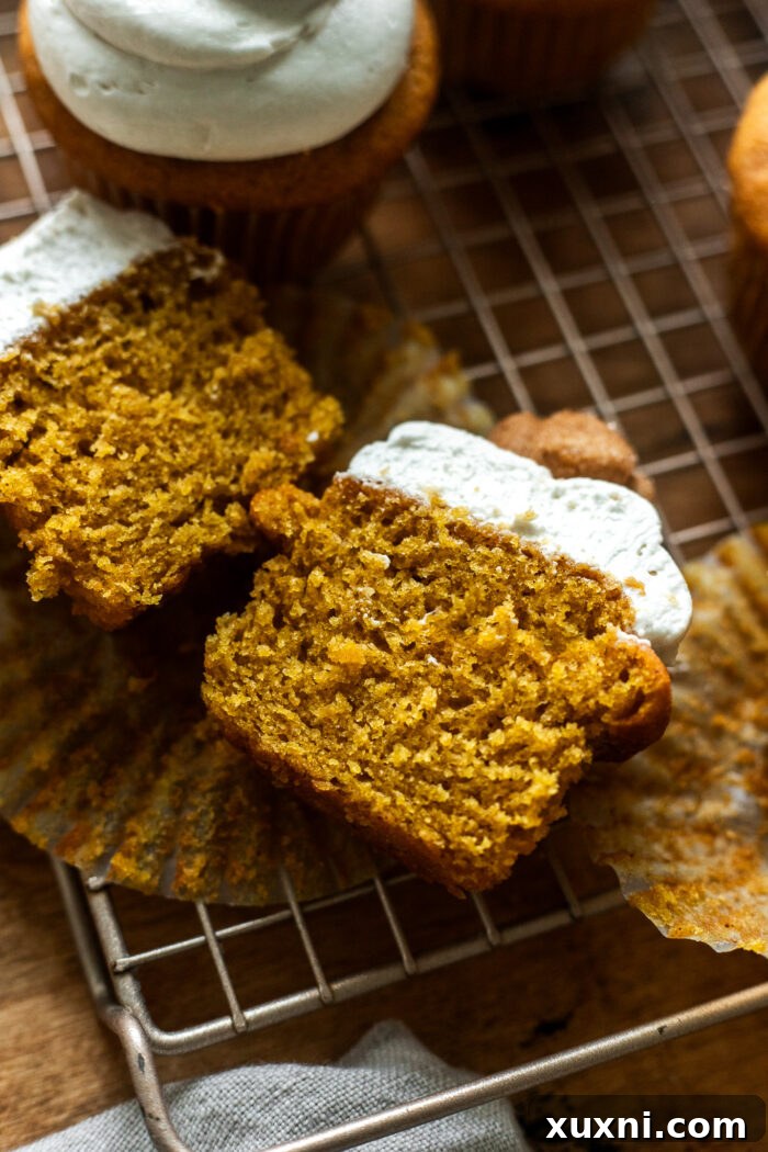 Sliced vegan pumpkin cupcake showing its moist interior and frosting layers.