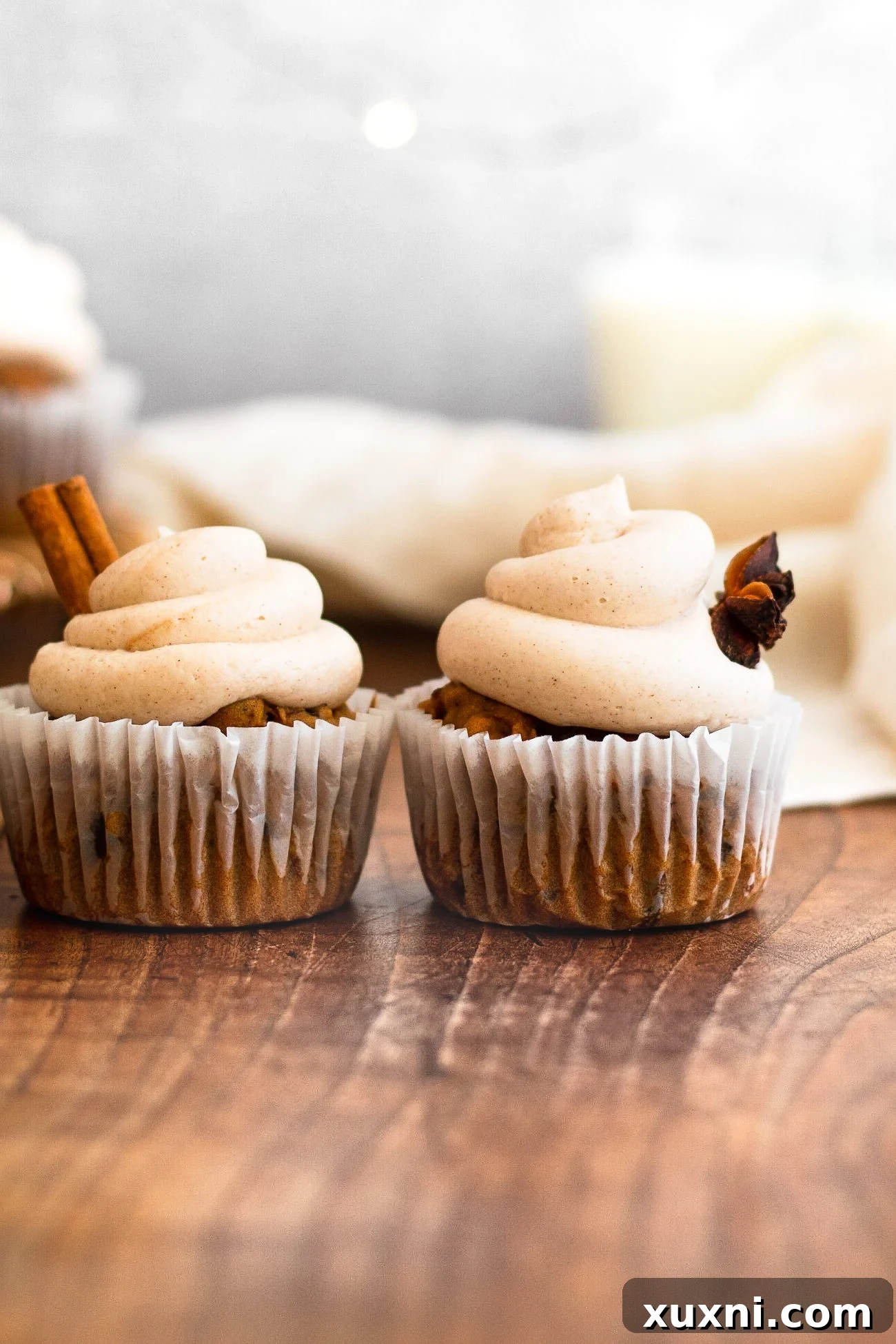 Close-up of three vegan cinnamon cupcakes on a wooden board, garnished with a sprinkle of cinnamon and a smooth swirl of vegan buttercream.