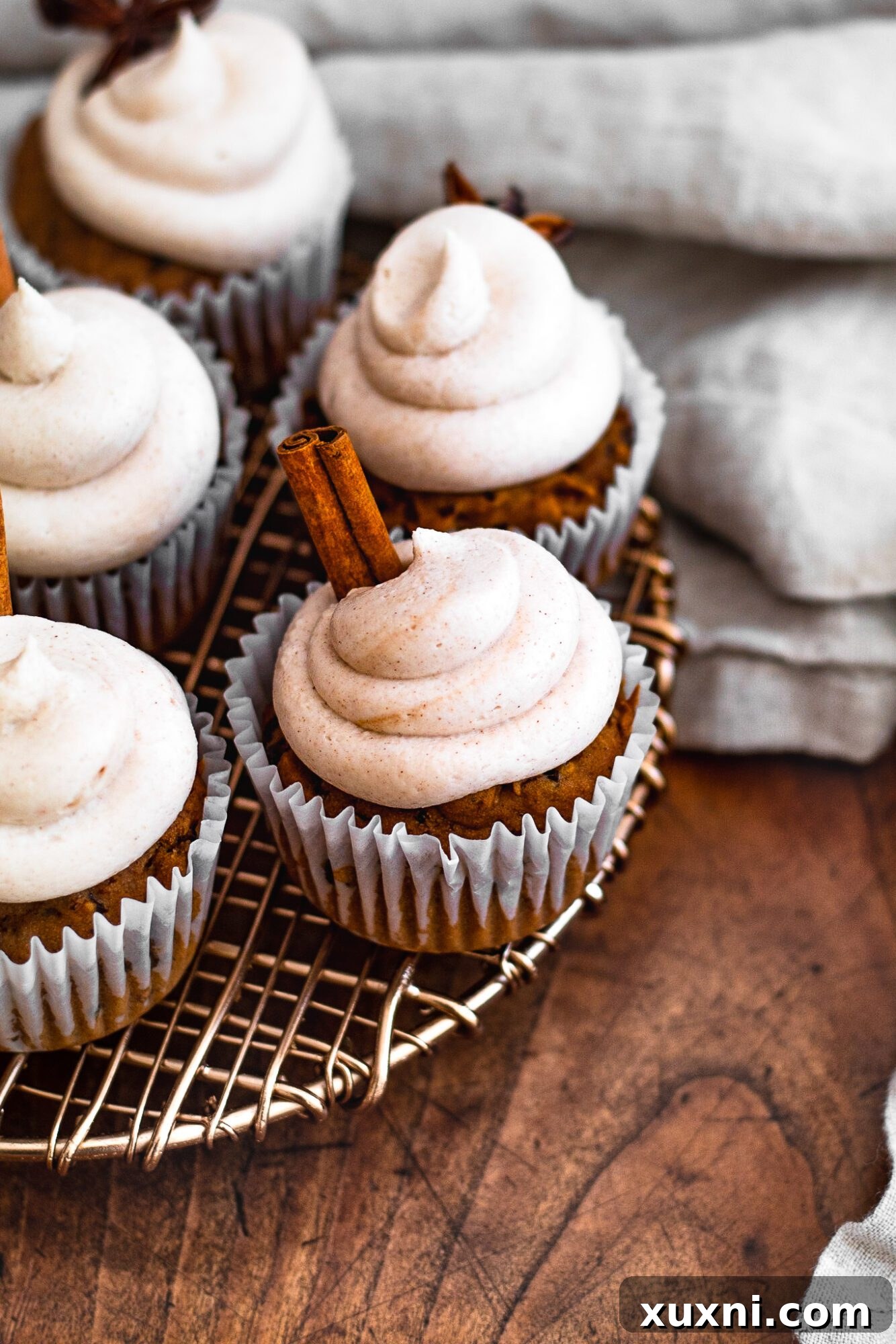 Overhead shot of several vegan cinnamon cupcakes arranged on a rustic wooden surface, highlighting their fluffy texture and cinnamon-dusted frosting.