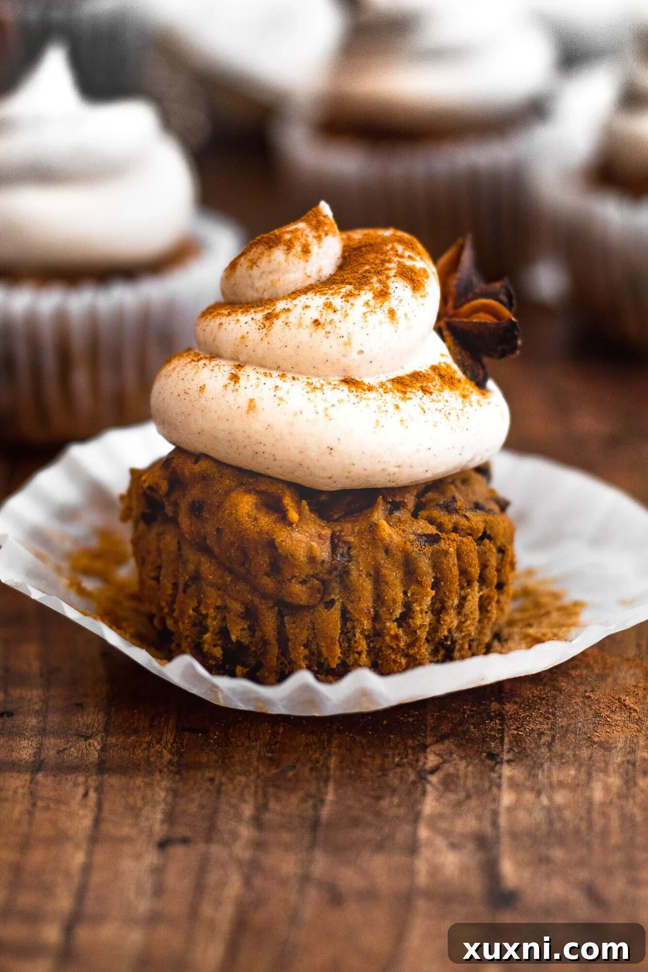 A single vegan cinnamon cupcake with a generous swirl of buttercream, dusted with extra cinnamon, presented on a light background.