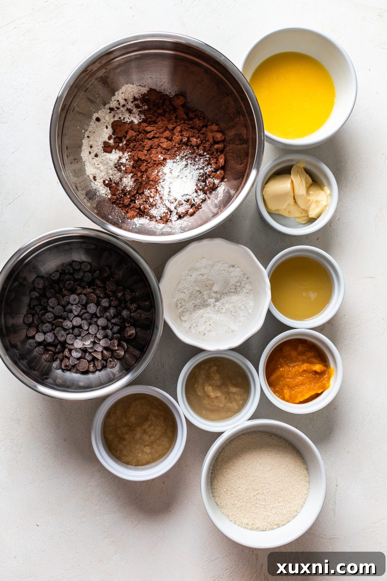 Arrangement of vegan pumpkin brownie ingredients including flour, cocoa powder, pumpkin puree, and chocolate chips.