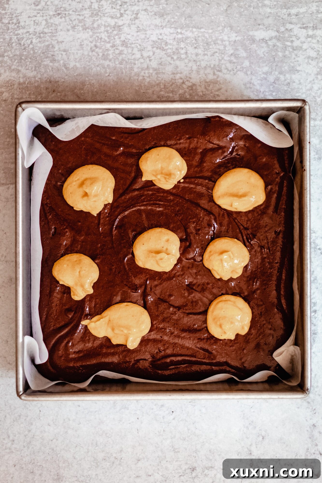 Close-up of pumpkin cheesecake swirl being gently added to brownie batter in a baking pan.