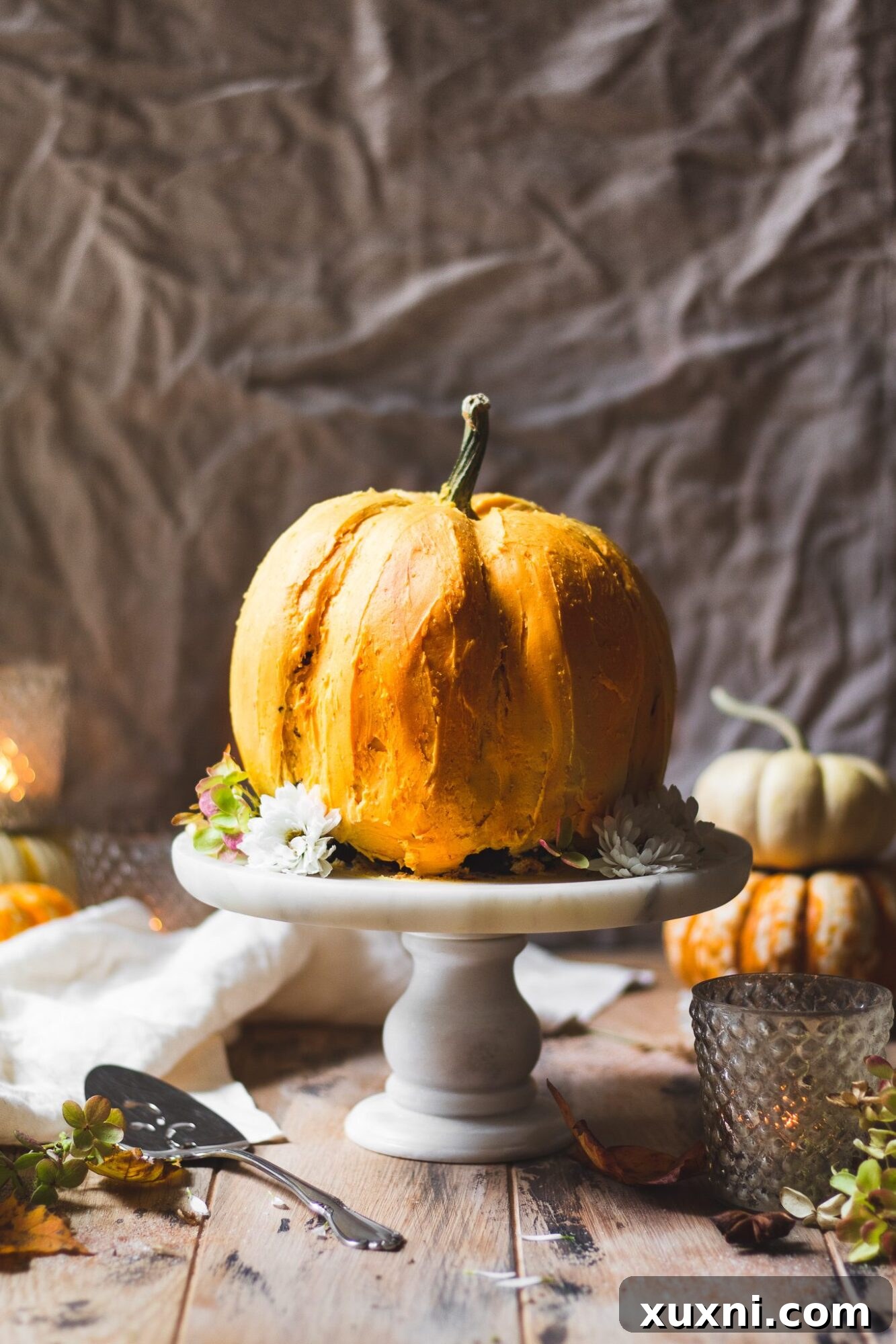A stunning pumpkin-shaped chocolate cake with dairy-free pumpkin spice buttercream frosting, displayed on a marble cake stand. Perfect for Fall celebrations.