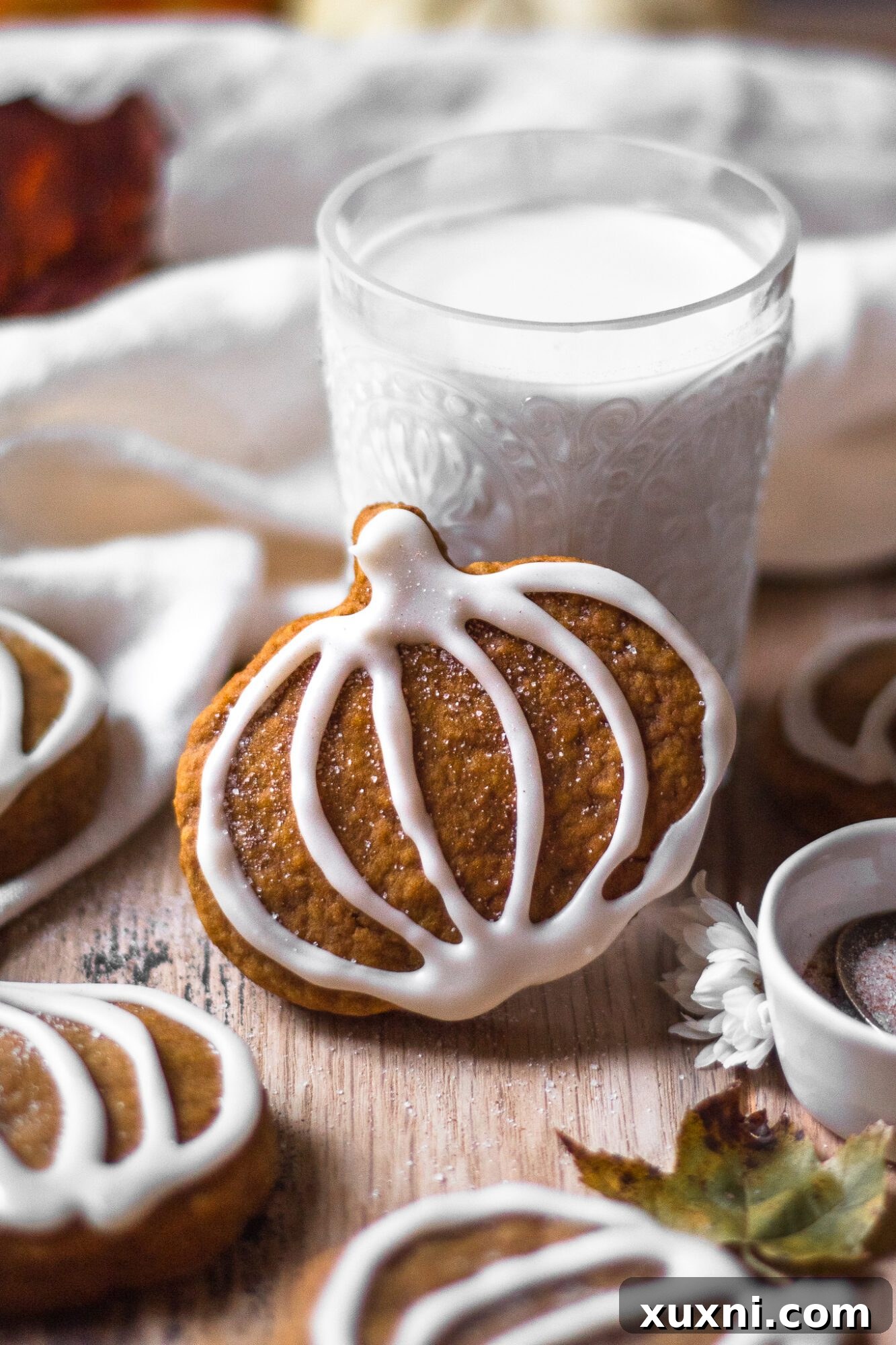 vegan pumpkin sugar cookie leaning against a glass of dairy-free milk