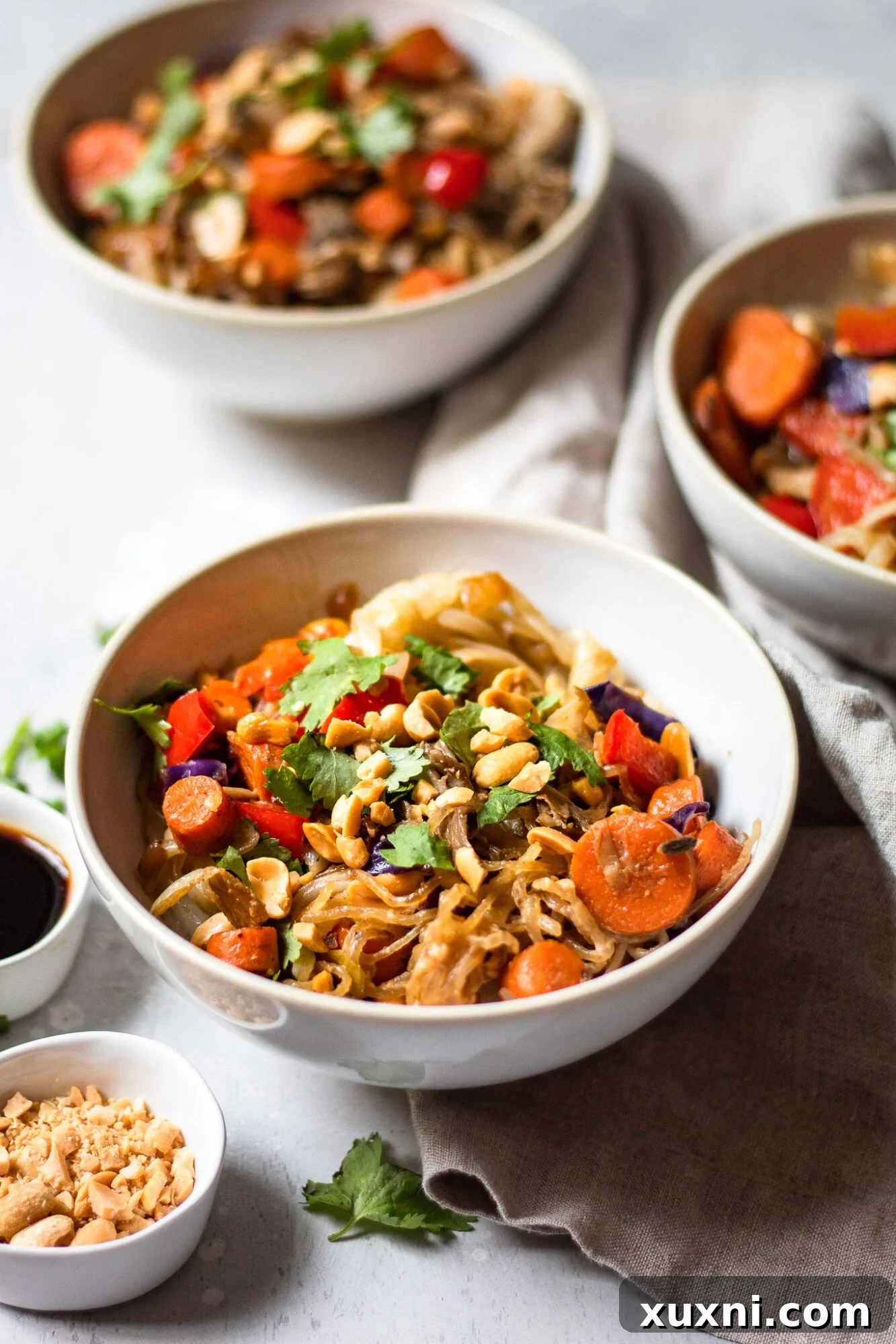 Three beautifully arranged bowls of vegan Pad Thai, showcasing the colorful ingredients and tantalizing sauce.