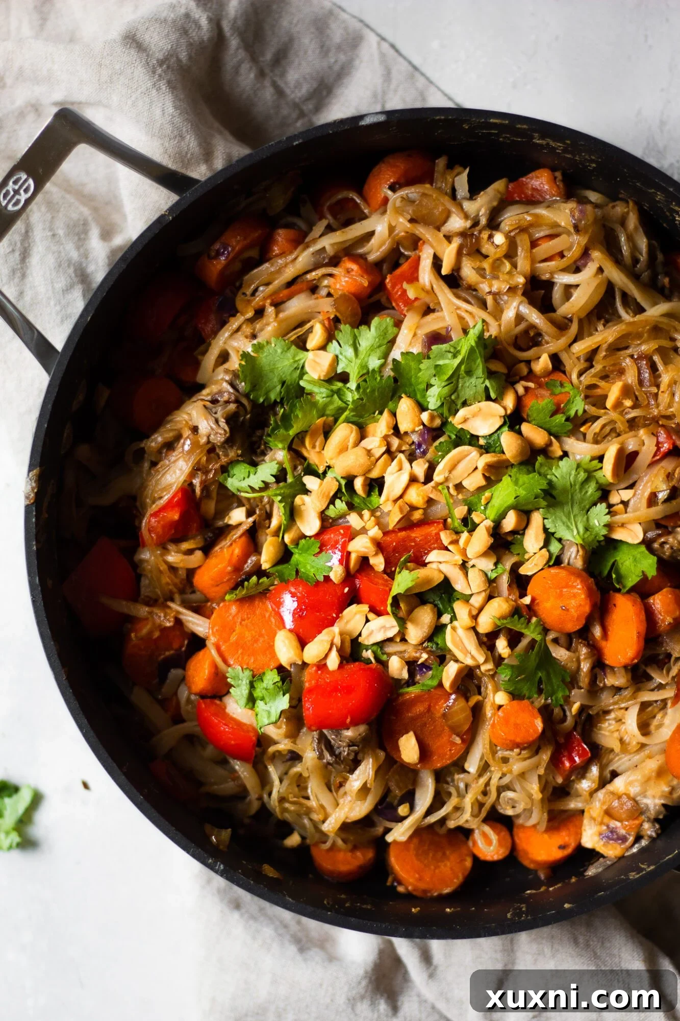 Close-up view of rice and kelp noodles being tossed with fresh vegetables in a large skillet, coated in a rich peanut sauce.