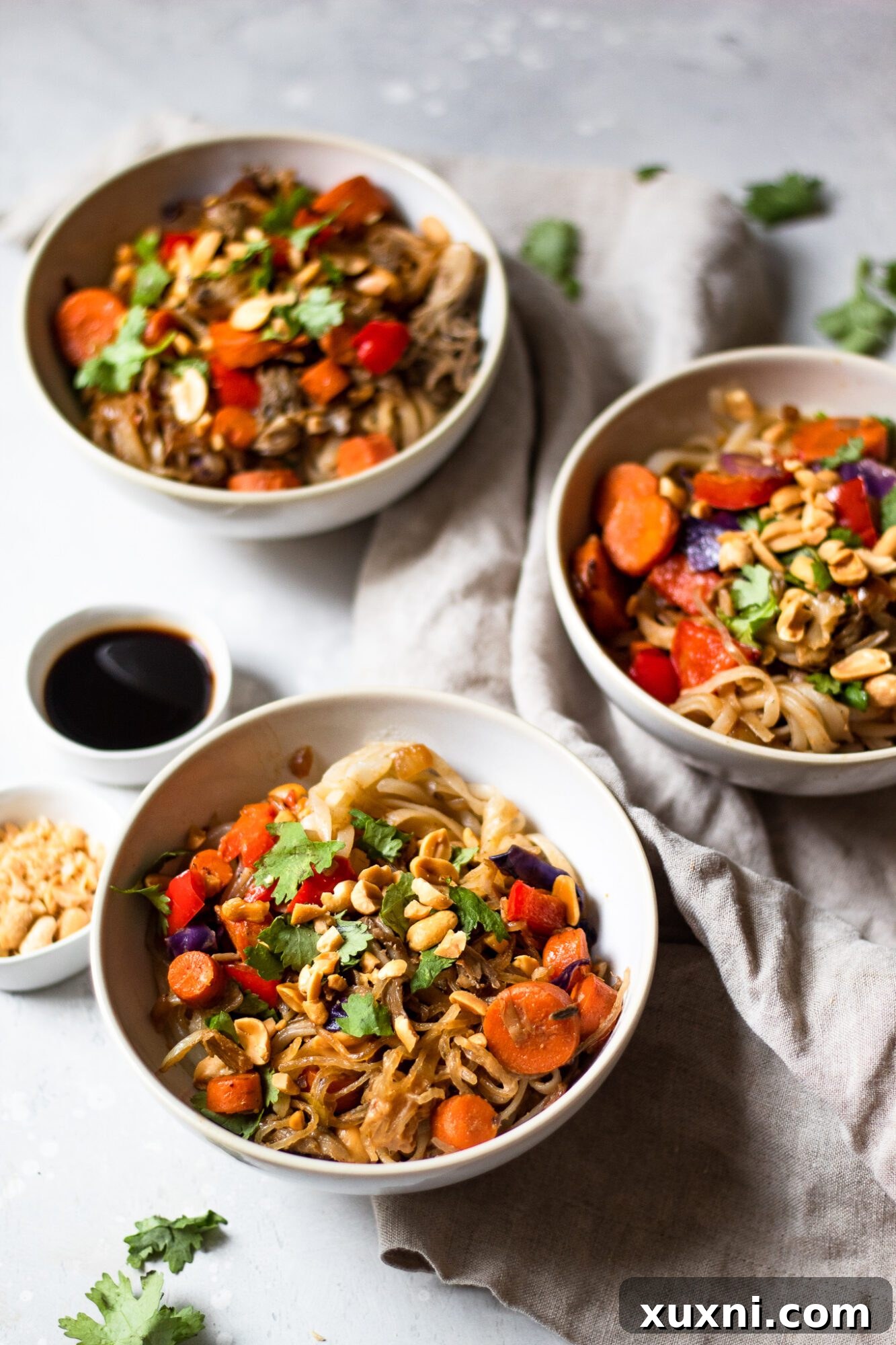 An appetizing view of three bowls of vegan Pad Thai, perfectly portioned and garnished, ready to be served.