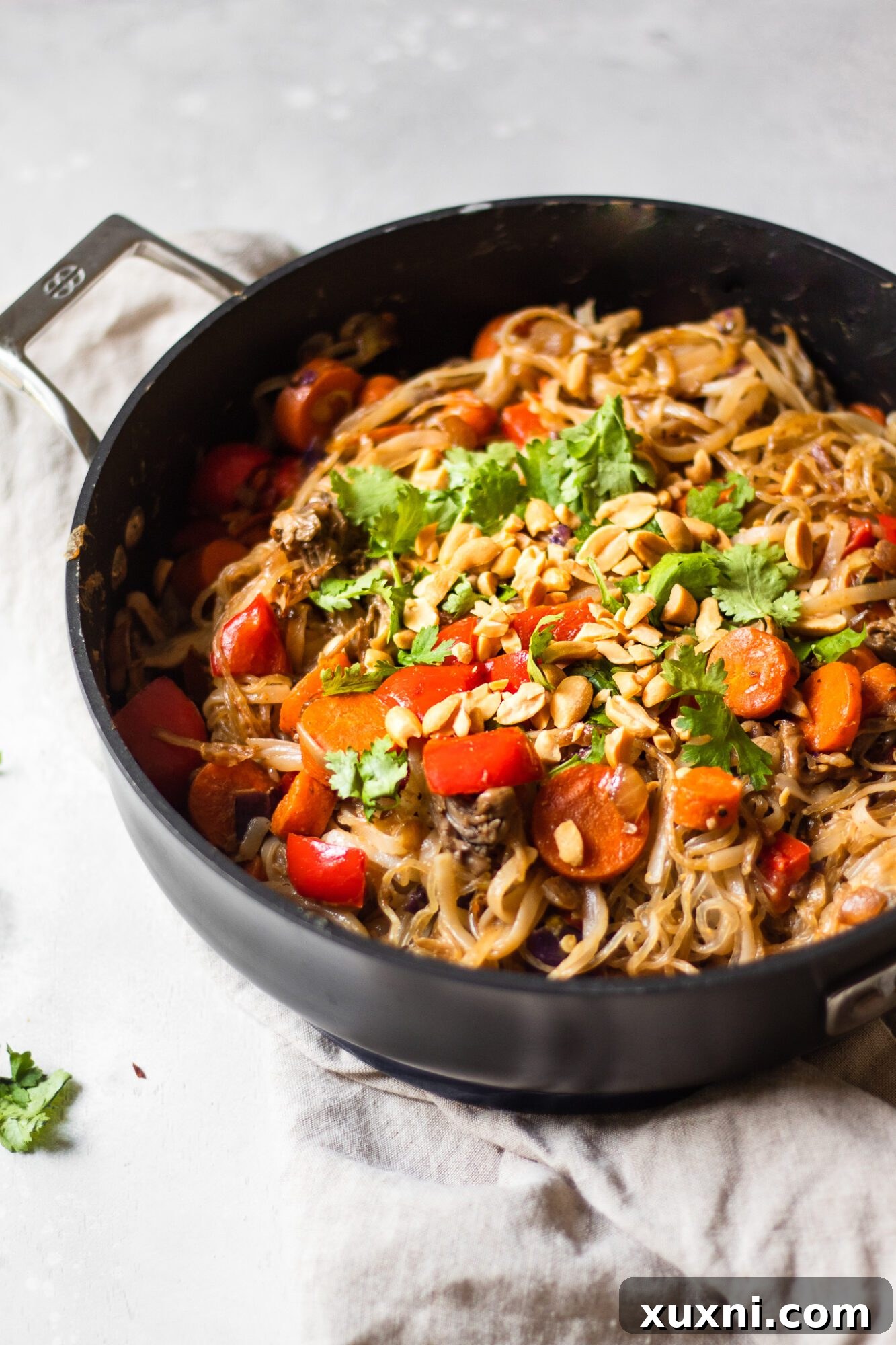 A large skillet filled with cooked rice and kelp noodles, fresh vegetables, and savory sauce, being mixed together.
