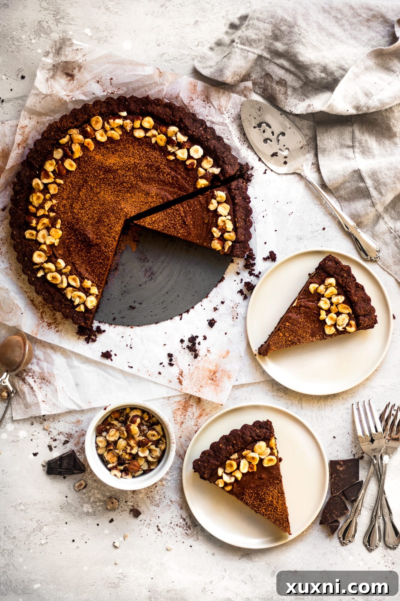 Presentation of vegan chocolate tart slices on a rustic wooden table, garnished with fresh fruit and hazelnuts