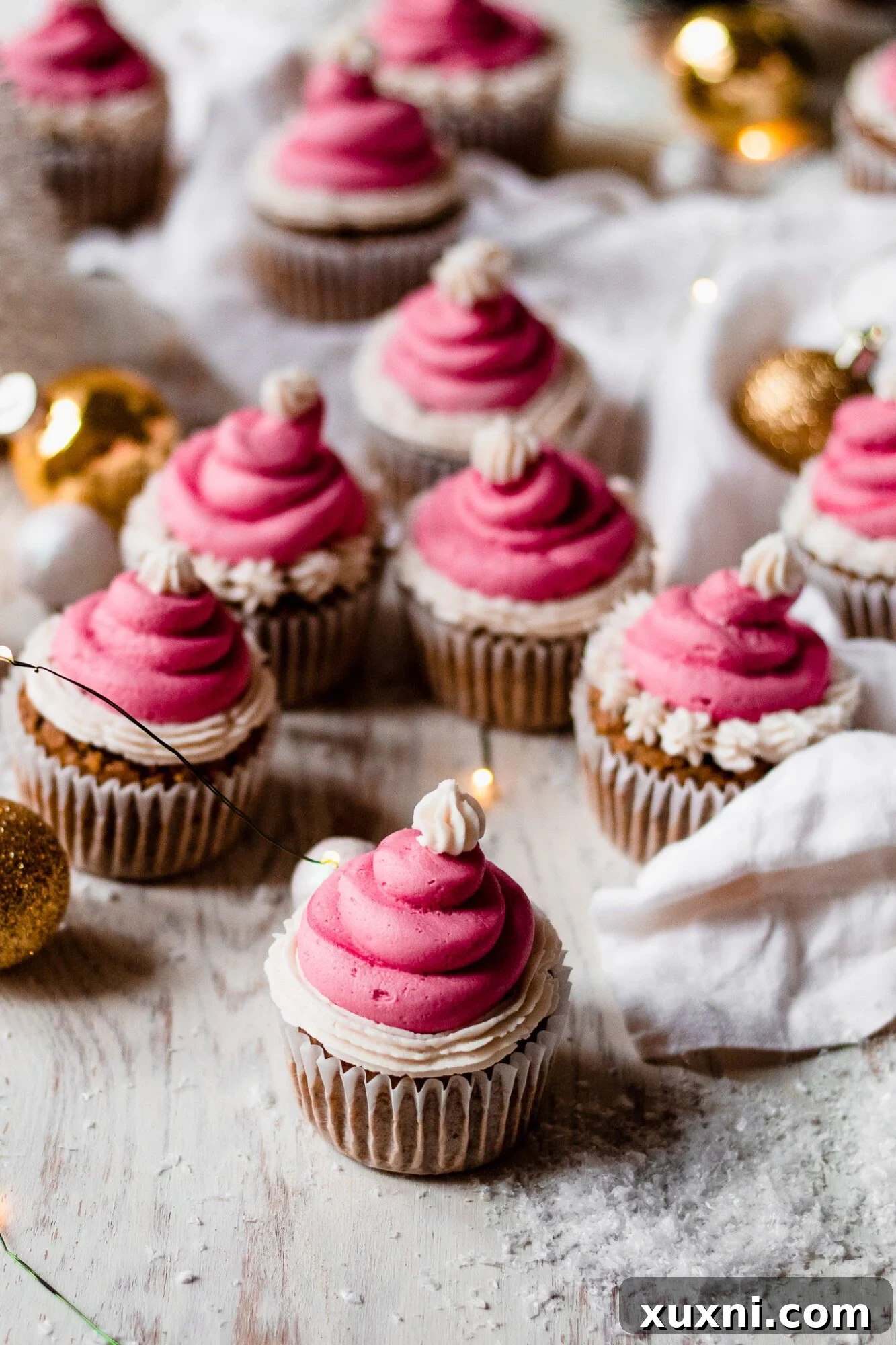 Festive Vegan Pistachio Santa Hat Cupcakes 3 Several vegan pistachio cupcakes arranged on a rustic wooden board, each adorned with a vibrant red Santa hat buttercream frosting and a white pom-pom.