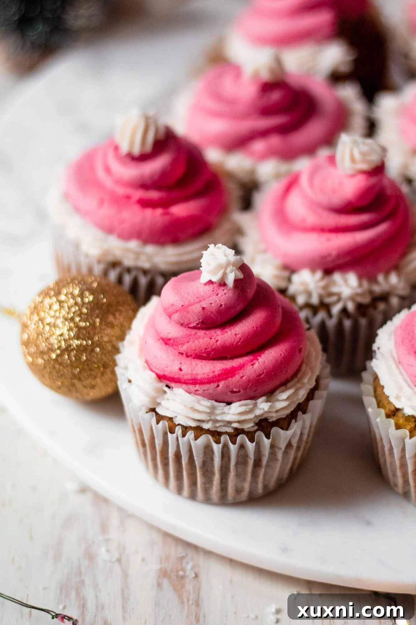 Festive Vegan Pistachio Santa Hat Cupcakes 5 A single vegan pistachio cupcake resting on a white marble plate, showcasing its green cake base and the start of a red and white Santa hat frosting.