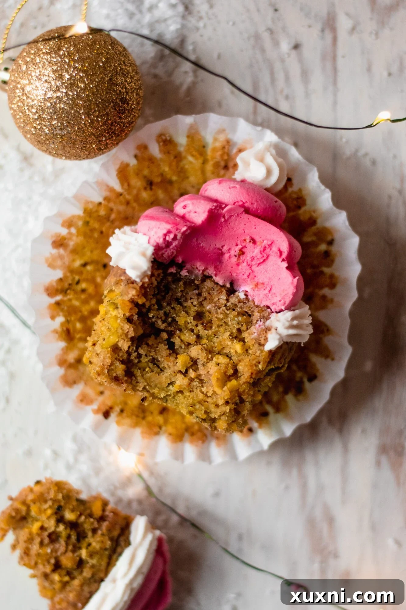 Festive Vegan Pistachio Santa Hat Cupcakes 6 A Christmas cupcake with a bite taken out, showcasing the moist green pistachio cake and the distinct layers of red and white Santa hat frosting.