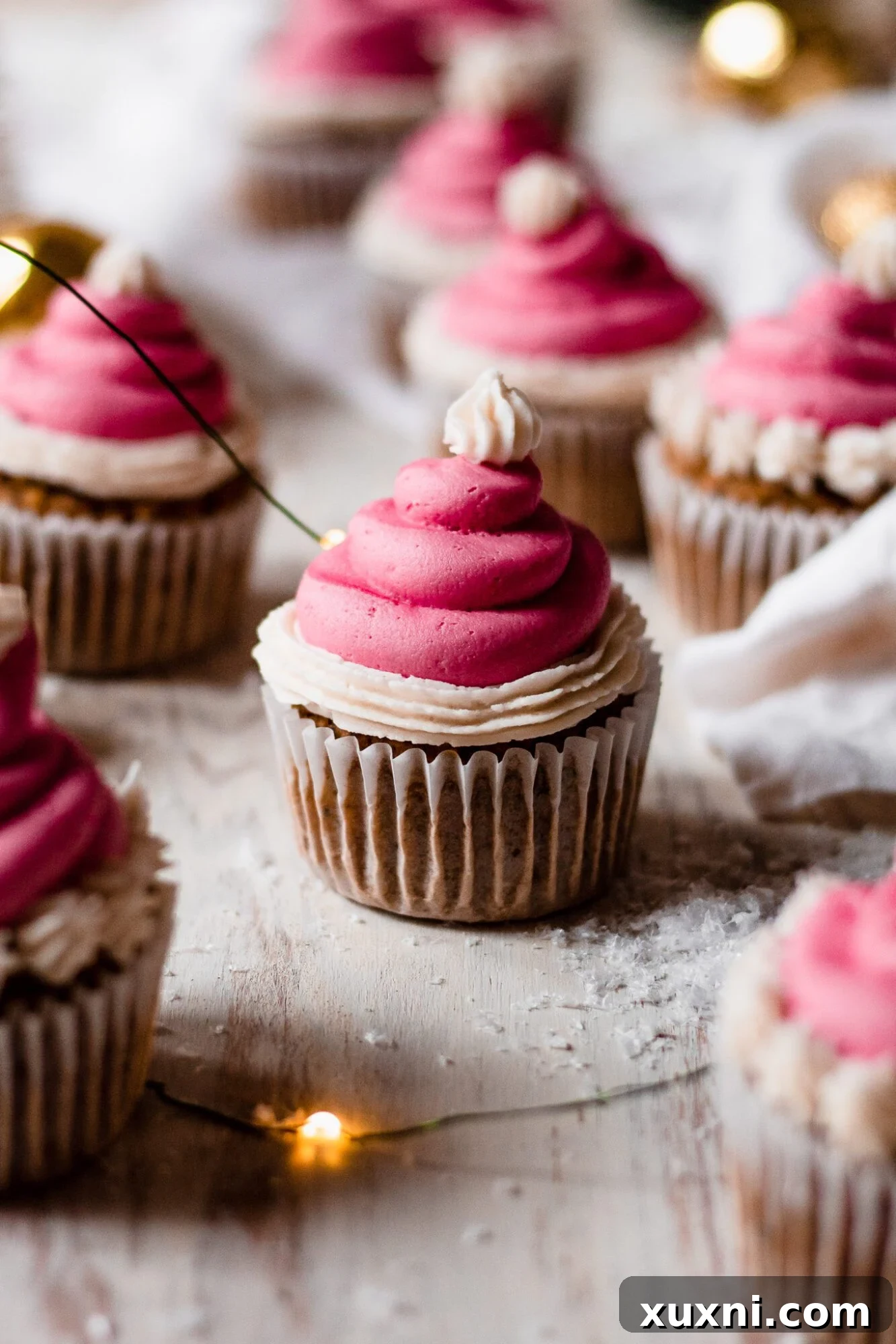 Festive Vegan Pistachio Santa Hat Cupcakes 10 Several festive Christmas cupcakes with Santa hat frosting, surrounded by warm, glowing string lights.
