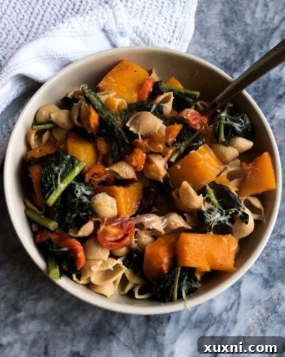 Butternut squash and kale pasta served in a rustic bowl, garnished with fresh herbs and vegan parmesan.