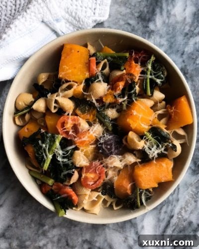Close-up of vibrant roasted butternut squash, kale, and cherry tomatoes on a baking sheet, ready to be mixed with pasta.