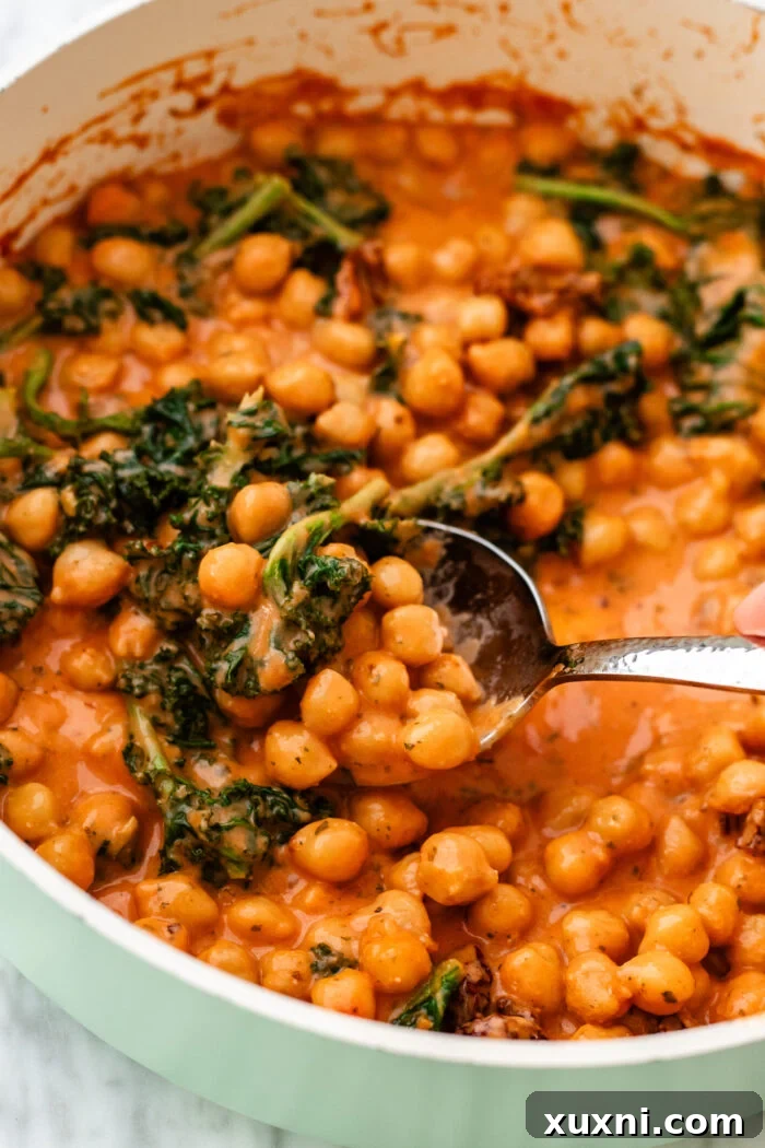 A serving spoon lifting a generous portion of creamy Marry Me Chickpeas from a skillet, showing off the rich sauce.