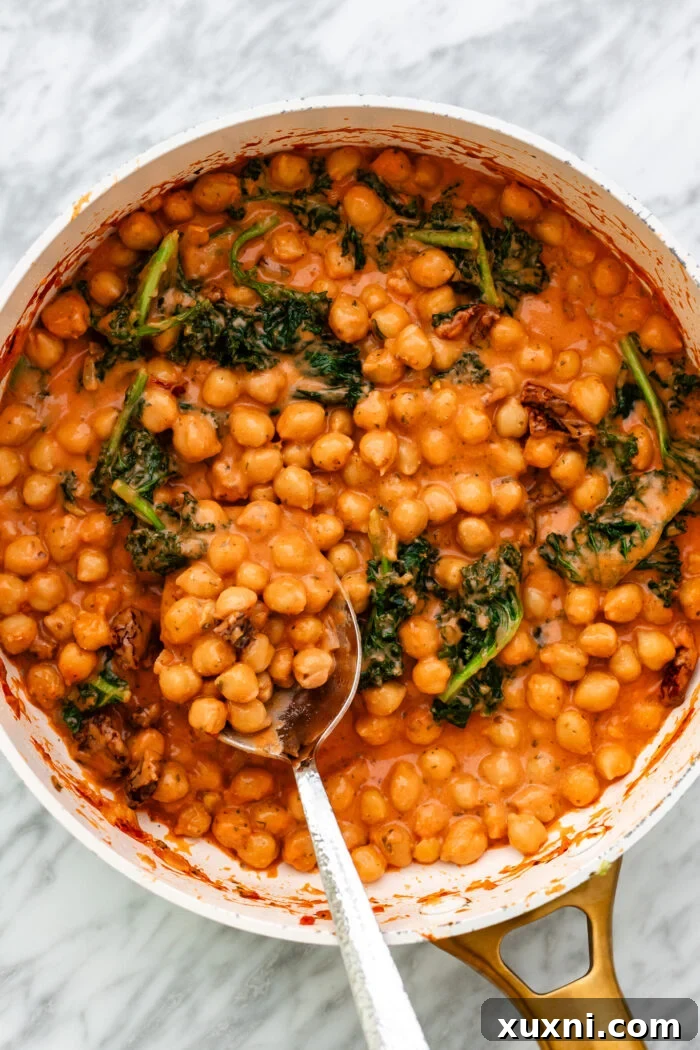 A large pot filled with the creamy and inviting Marry Me Chickpeas, garnished with fresh herbs, in a kitchen setting.