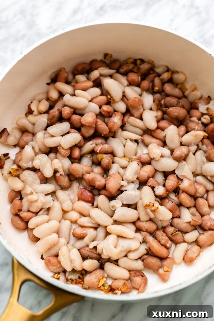Shallots, minced garlic, and butter beans sautéing in a pan with olive oil.