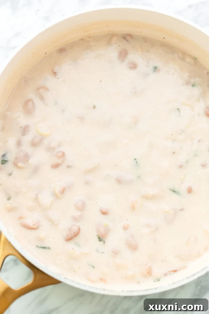 Lemon creamy sauce mixture being poured over butter beans in a pot before thickening.