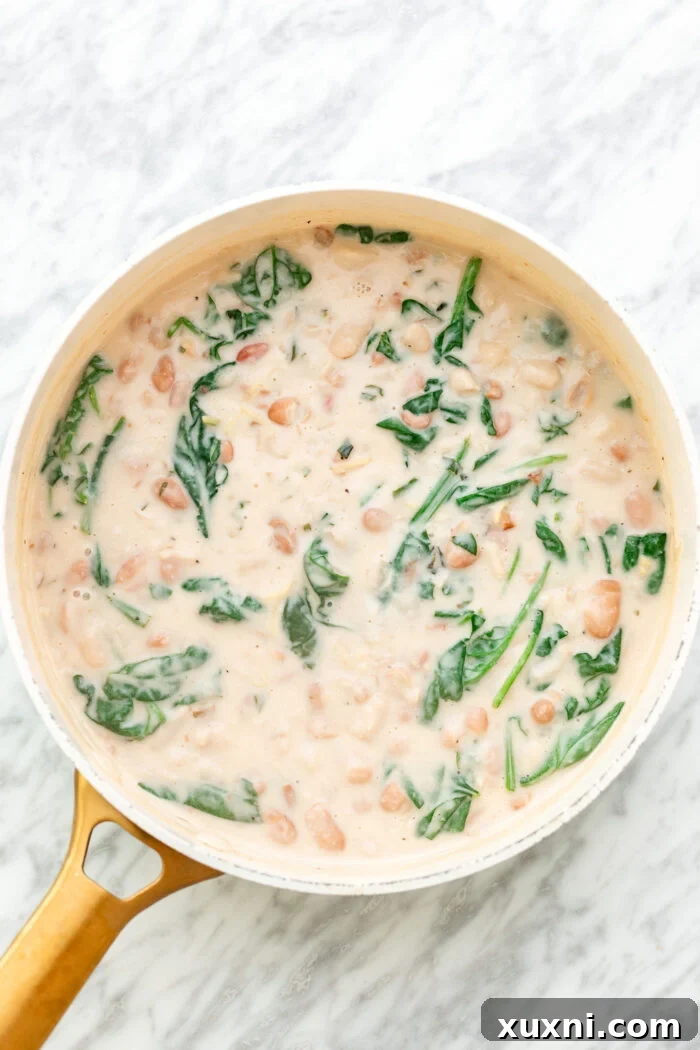 Thickened lemon creamy sauce with wilted spinach mixed into butter beans in a pot.