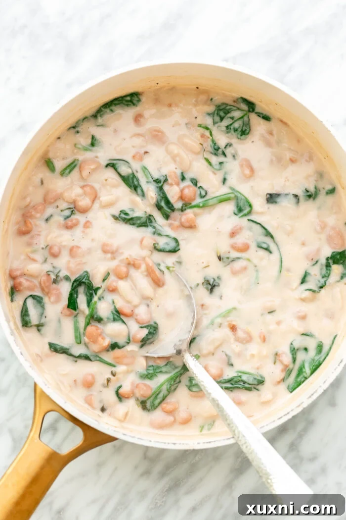 A serving of creamy lemon butter beans with spinach in a bowl, garnished with lemon slices and fresh herbs.